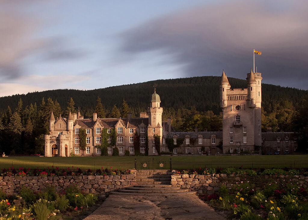 Balmoral castle with a flag on a hillside under a cloudy sky