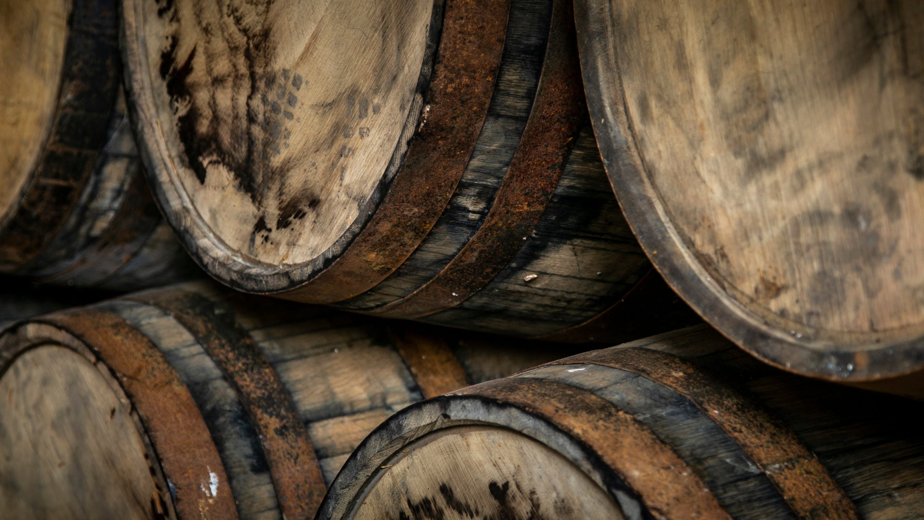 Close-up of stacked wooden barrels with dark metal hoops, showing weathered wood grain and stained surfaces.